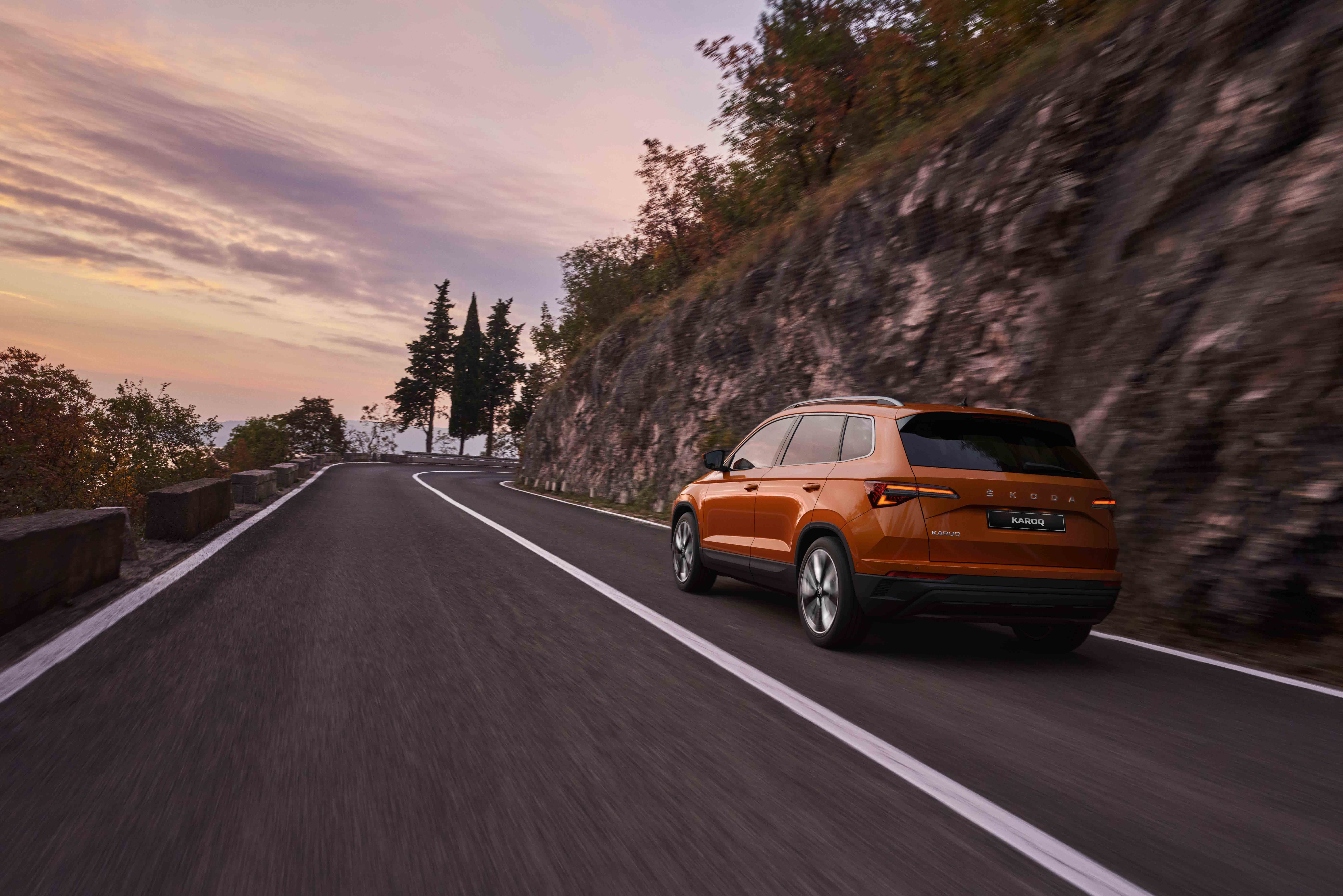 Rear view of Orange Škoda Karoq driving on scenic road