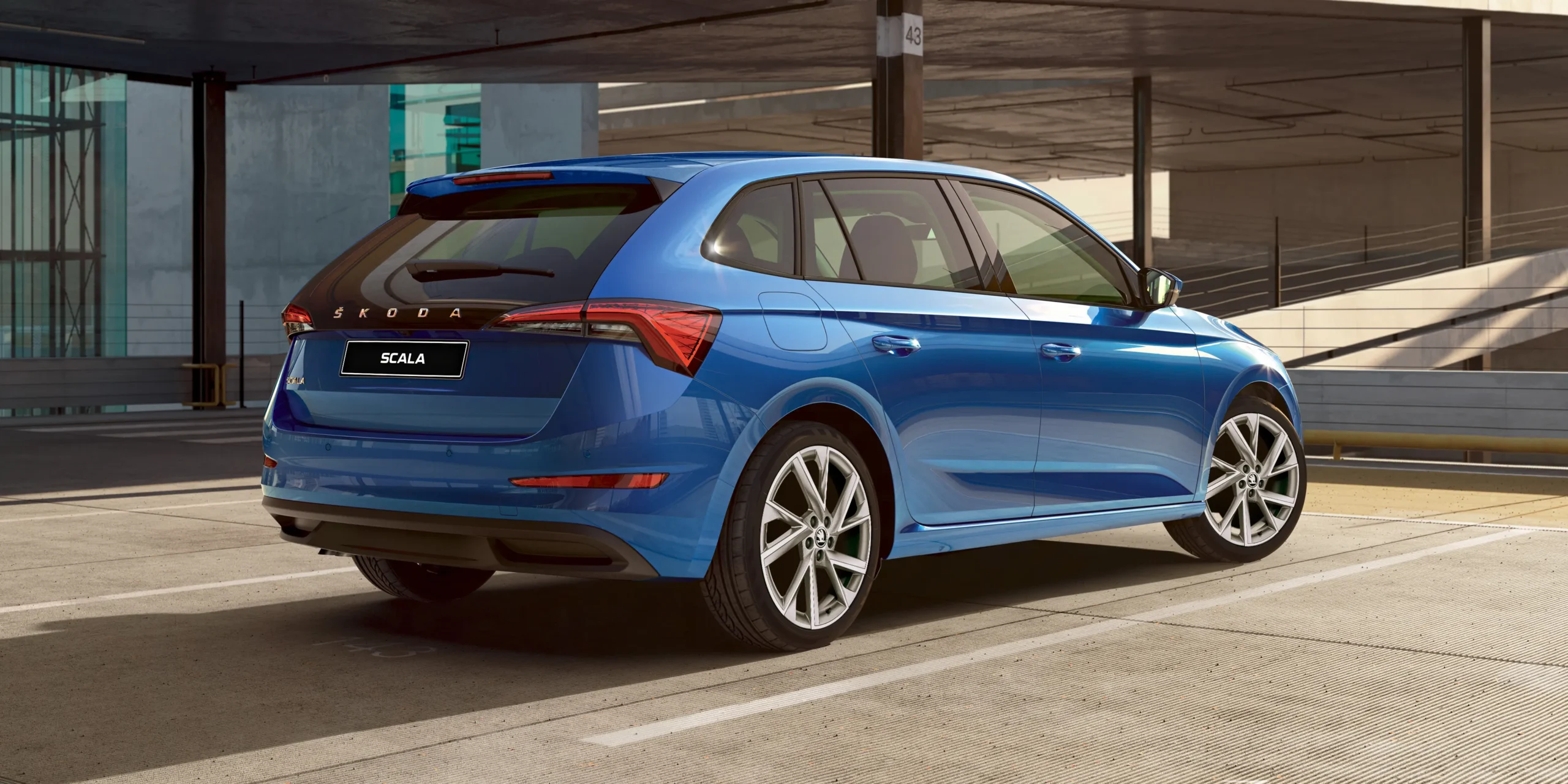 Rear view of the Škoda Scala in metallic blue, highlighting its sleek taillight design, sculpted hatch, alloy wheels, and sporty European styling
